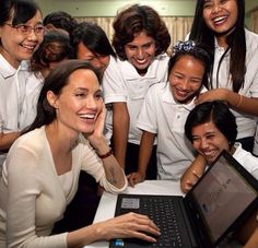 a group of women standing around a laptop on a table with one woman smiling at the camera