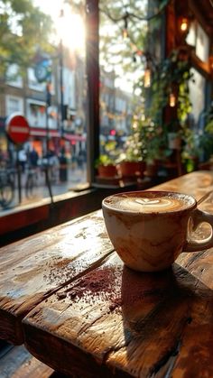 a cup of coffee sitting on top of a wooden table in front of a window