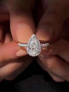 a woman's hand holding an engagement ring with a pear shaped diamond on it