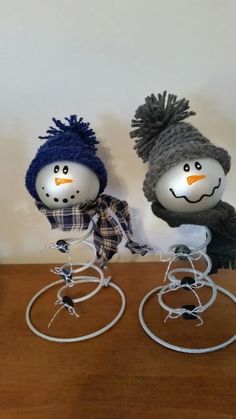 two snowmen with hats and scarves on top of a wooden table in front of a white wall