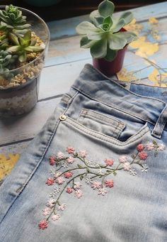 a pair of jeans with embroidered flowers on them and a succulent potted in the back