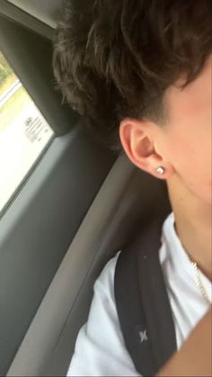 a young man sitting in the back seat of a car with ear piercings on