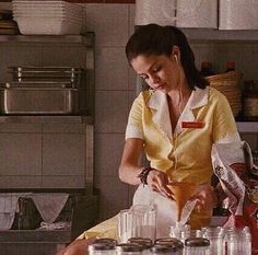 a woman standing in a kitchen preparing food on top of a counter next to jars