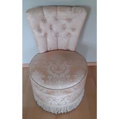 an upholstered chair with tassels on the back and foot rests against a wall