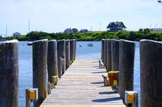 a wooden dock leading to a house on the water with boats floating in the background