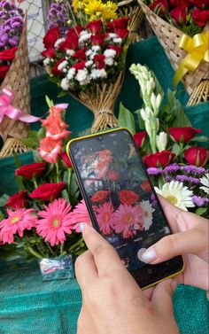 a person holding a cell phone in their hand near many colorful flowers on the table