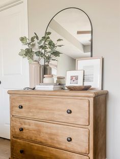 a dresser with a mirror, plant and pictures on it