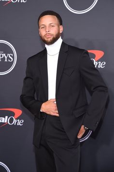 a man with a beard wearing a black suit and white turtle neck sweater at an event