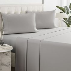 a white bed with grey sheets and pillows