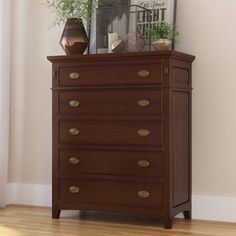 a wooden dresser sitting on top of a hard wood floor next to a mirror and potted plant