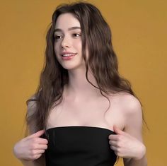 a woman with long brown hair wearing a black strapless dress and posing for the camera