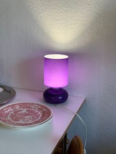 a table with a purple lamp and plate on it, next to a cd player