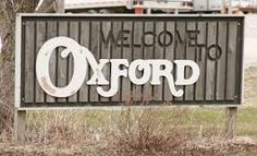 a sign that says welcome to oxford on the side of a road in front of a truck