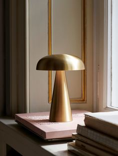 a gold lamp sitting on top of a table next to a book and window sill