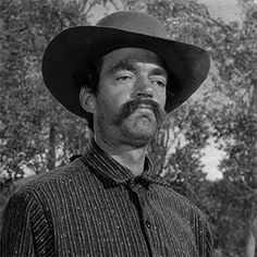 a man wearing a cowboy hat standing in front of trees