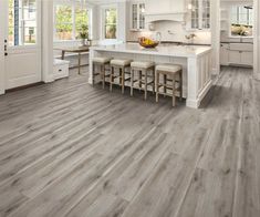 a large kitchen with white cabinets and wood flooring, along with an island in the middle