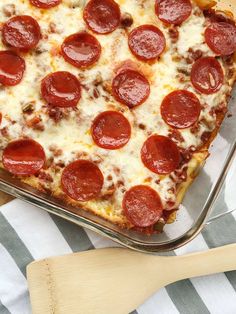 a pepperoni pizza sitting on top of a pan next to a wooden spatula