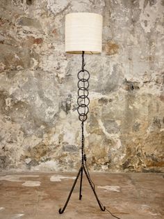 a floor lamp with a white shade on it in front of a stone wall and concrete floor