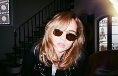 a woman wearing sunglasses standing next to a stair case in a room with dark walls