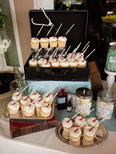 cupcakes are arranged on sticks in front of an open suitcase at a party