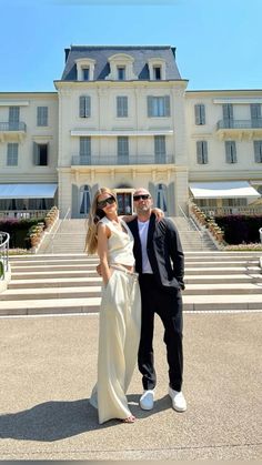 a man and woman standing in front of a large white building with steps leading up to it