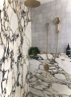 a bathroom with marble walls and flooring that has gold faucets on the shower head