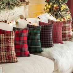 christmas pillows on a couch in front of a fireplace with trees and lights behind them