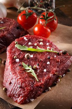 two pieces of raw meat sitting on top of a piece of paper next to tomatoes