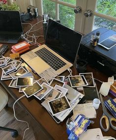 there are many pictures on the desk with laptops and other items scattered around it