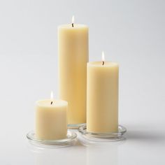 three white candles sitting next to each other on top of a glass table with one candle lit