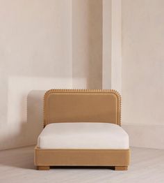 an upholstered bed with white sheets and pillows in front of a beige wall