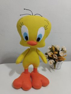 a yellow stuffed bird with blue eyes and orange feet next to a basket of flowers