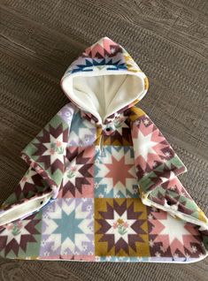 a multicolored jacket with an open hood on top of a wooden floor next to a pair of scissors