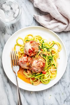 a white plate topped with pasta and meatballs next to a glass of water on a marble table