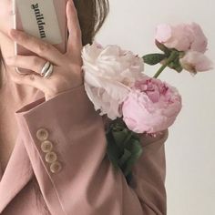 a woman holding a cell phone up to her face with flowers in front of her