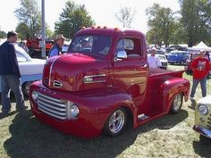 an old red truck parked on top of a grass covered field next to other cars