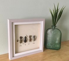 three rocks in a white frame sitting next to a green vase on a wooden table