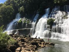 people are standing at the base of a waterfall