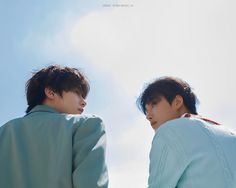 two young men standing next to each other in front of a blue sky with clouds