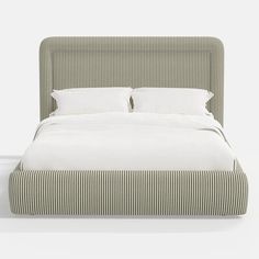 an upholstered bed with two pillows and white linens on the headboard