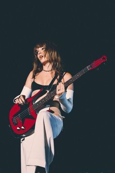 a woman holding a red guitar in her right hand and posing for the camera on stage