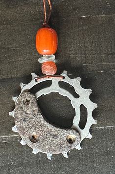 a bicycle chainring with an orange bead hanging from it's center sprock