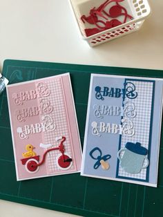 two baby shower cards sitting on top of a cutting board next to scissors and other items