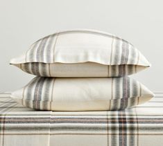 two pillows sitting on top of a bed with white sheets and checkered pillow cases