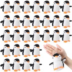 a hand is holding a stuffed penguin with many penguins in the background