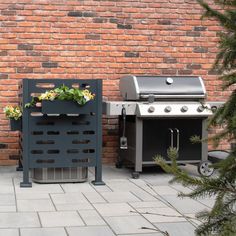 an outdoor grill with flowers on it next to a brick wall