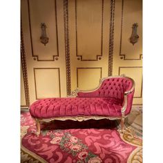 a pink couch sitting on top of a rug in front of a wall with gold trim