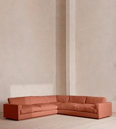 an orange sectional sofa in front of a white wall and wooden floor, with one corner facing the couch