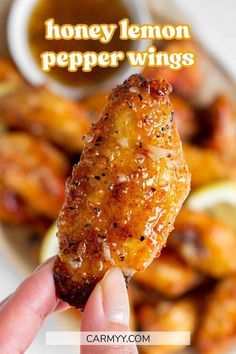 a hand holding up a piece of chicken with honey lemon pepper wings in front of it