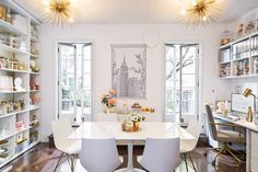 a white dining room table surrounded by chairs and open shelving units with gold accents